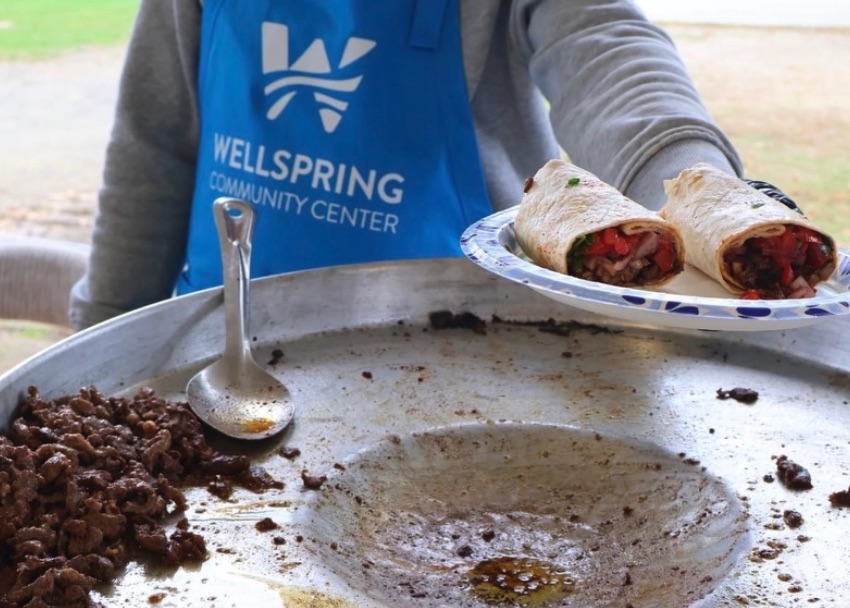 A volunteer in a Wellspring apron serving food at a community event